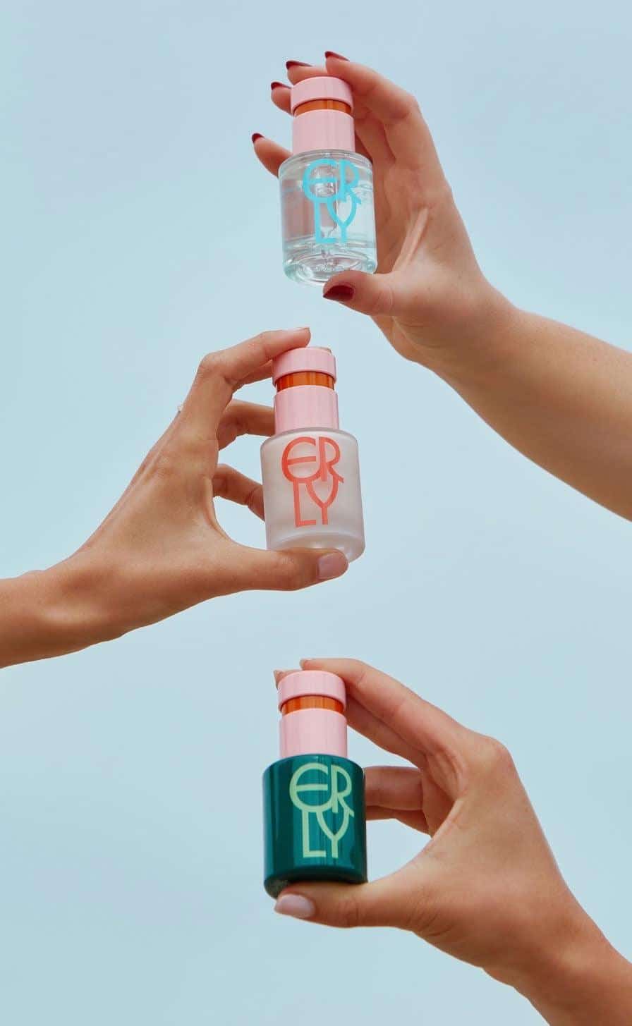 Three small bottles with colorful labels held by hands against a light blue background