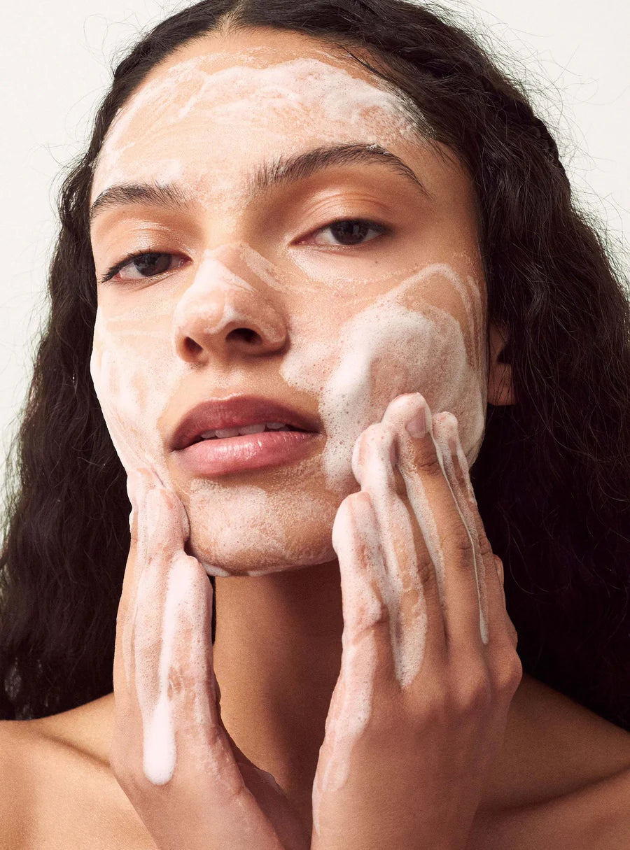 Woman applying a facial mask to her face with a neutral background